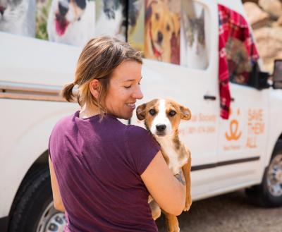 Smiling person holding a puppy next to a pet transport van