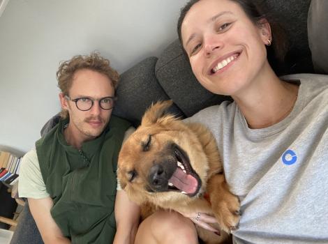Kimchi the dog lying on a couch with Hadley and Gereth, all smiling